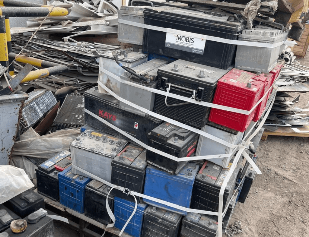 Scrap auto batteries buyers in Dubai - Used car and truck batteries stacked in an industrial scrapyard for recycling and resale.